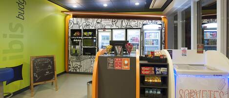 Una cafetería con un menú en la pizarra, una máquina de café y una exhibición de aperitivos y bebidas.