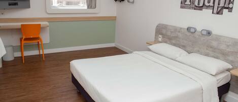 A bedroom with a bed, a desk, a chair, a TV, and a window with curtains.