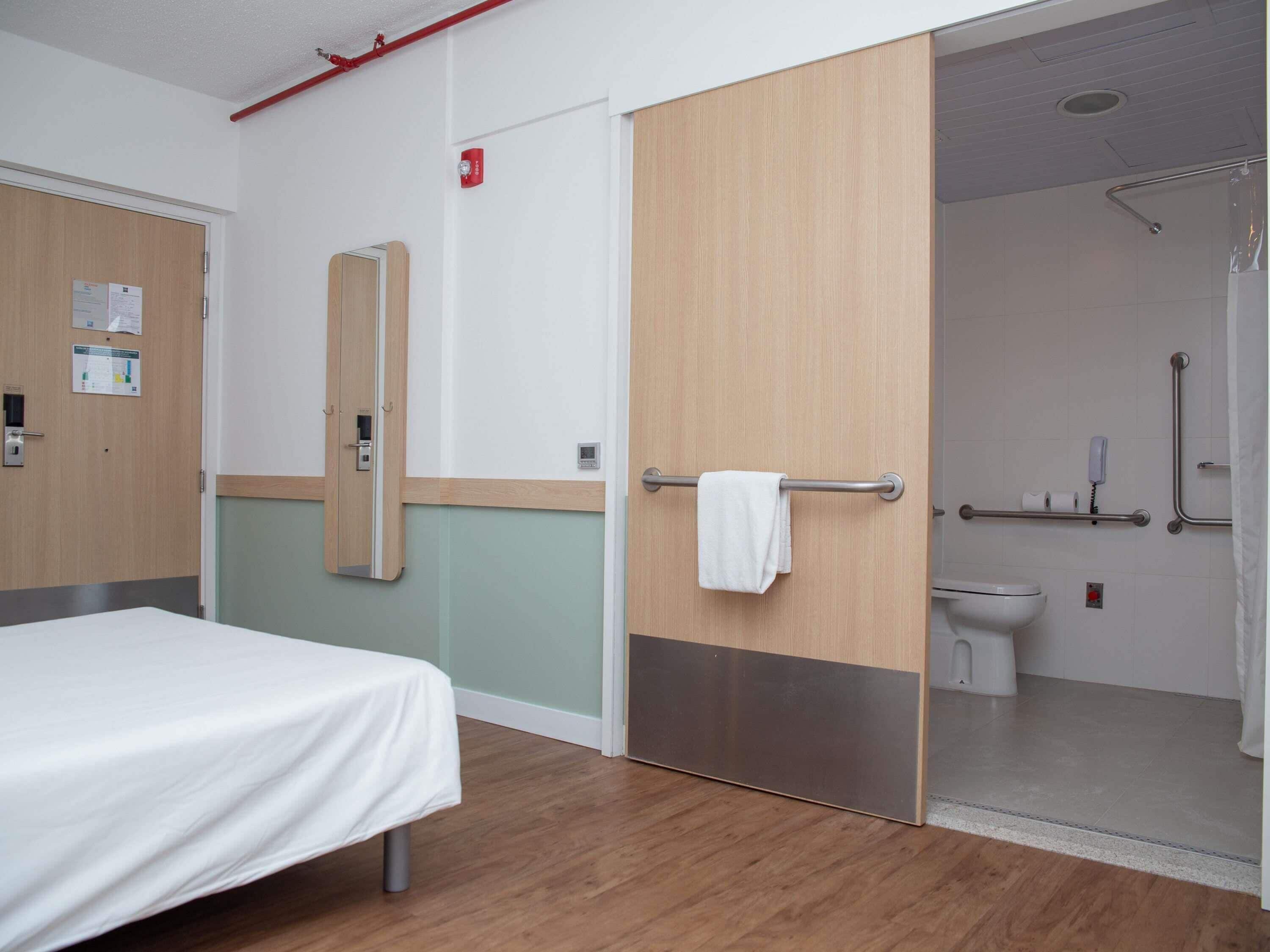 A hotel room with a bed, a bathroom with a shower, and a mirror.