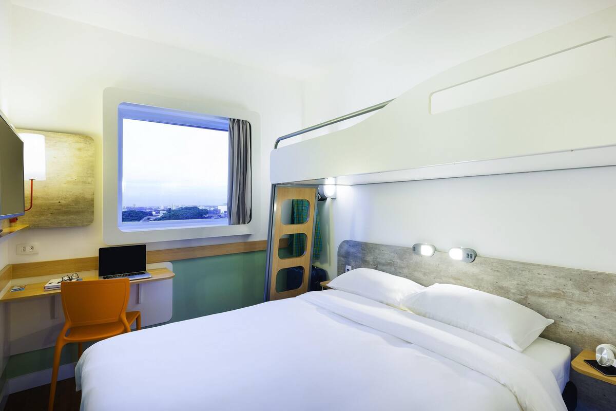 Une chambre d’hôtel avec un lit, un bureau, une chaise et une fenêtre donnant sur un paysage agréable.