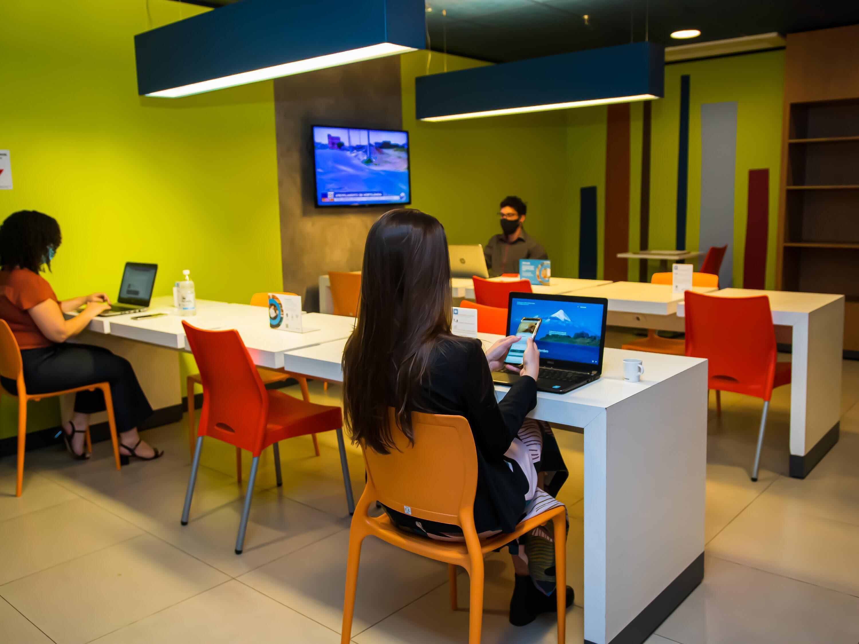 A modern office space with white desks, orange chairs, and a person using a laptop.