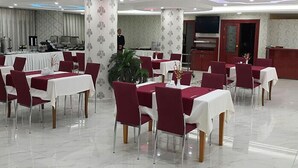 A dining area with tables set for service, a kitchen in the background, and a modern ceiling design. - Miroglu Hotel (Diyarbakir)