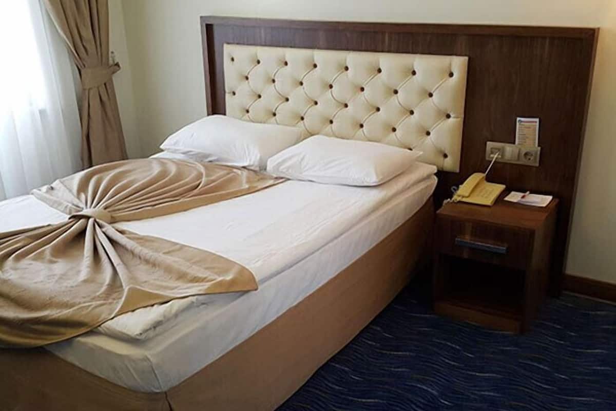 Habitación de hotel con una cama grande, cabecera de madera, mesita de noche con teléfono y alfombra azul.