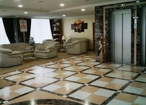 A lobby with a checkered floor, sofas, a bookshelf, and a marble column. - Miroglu Hotel (Diyarbakir)