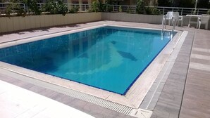 A rectangular swimming pool with clear blue water, surrounded by a tiled deck and a low wall. - Miroglu Hotel (Diyarbakir)