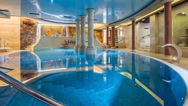 An indoor swimming pool with a curved design, surrounded by stone walls and columns, and a tiled floor. - VacationClub - Nadbrzeżna Apartments (Mielno)