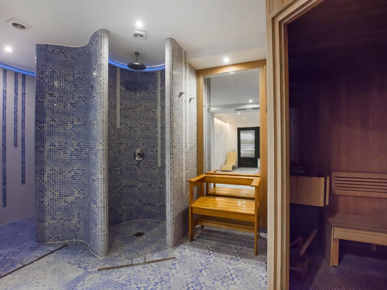 Et moderne badeværelse med bruseområde, mosaikvægge og en træbænk.