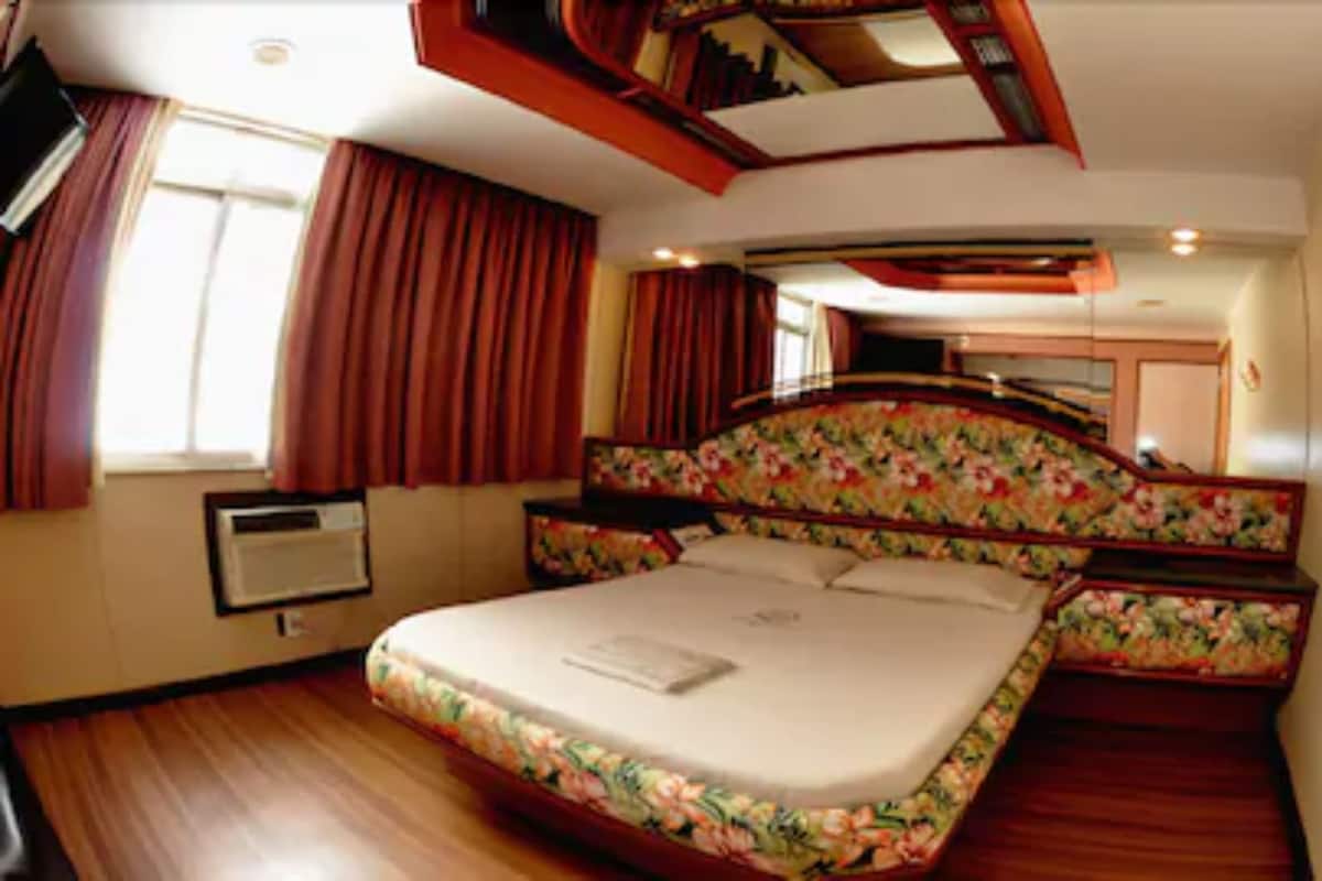 Un dormitorio con una cama grande, cabecera de madera, una ventana con cortinas y un aire acondicionado instalado.