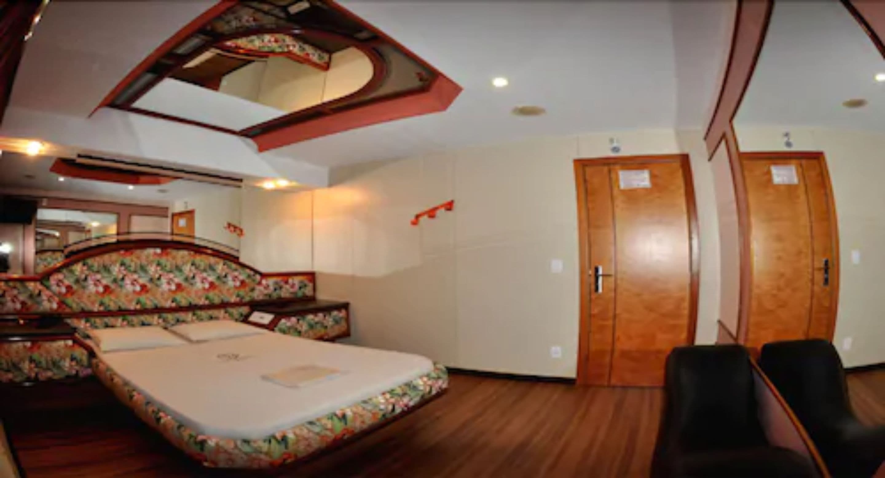 A hotel room with a bed, a desk, two chairs, a wardrobe, and a mirror.