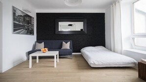 Ett modernt rum med en svart tegelvägg, en vit soffa, ett litet vitt bord, en vit säng och ett stort fönster.