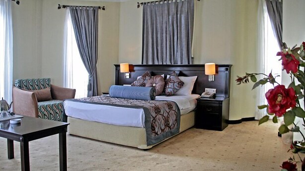 Quarto de hotel com cama, mesas de cabeceira, uma cadeira, escrivaninha e um vaso de flores.