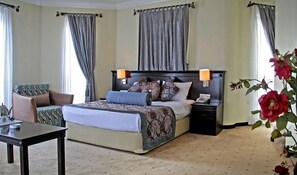 Une chambre d’hôtel avec un lit, des tables de chevet, une chaise, un bureau et un vase de fleurs.