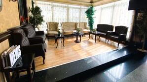 Um hall amplo com sofás de couro, uma mesa de centro e um balcão de recepção com suporte para jornais.