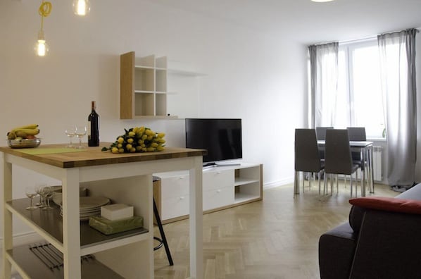A modern living room with a dining area, a TV, and a window with curtains.