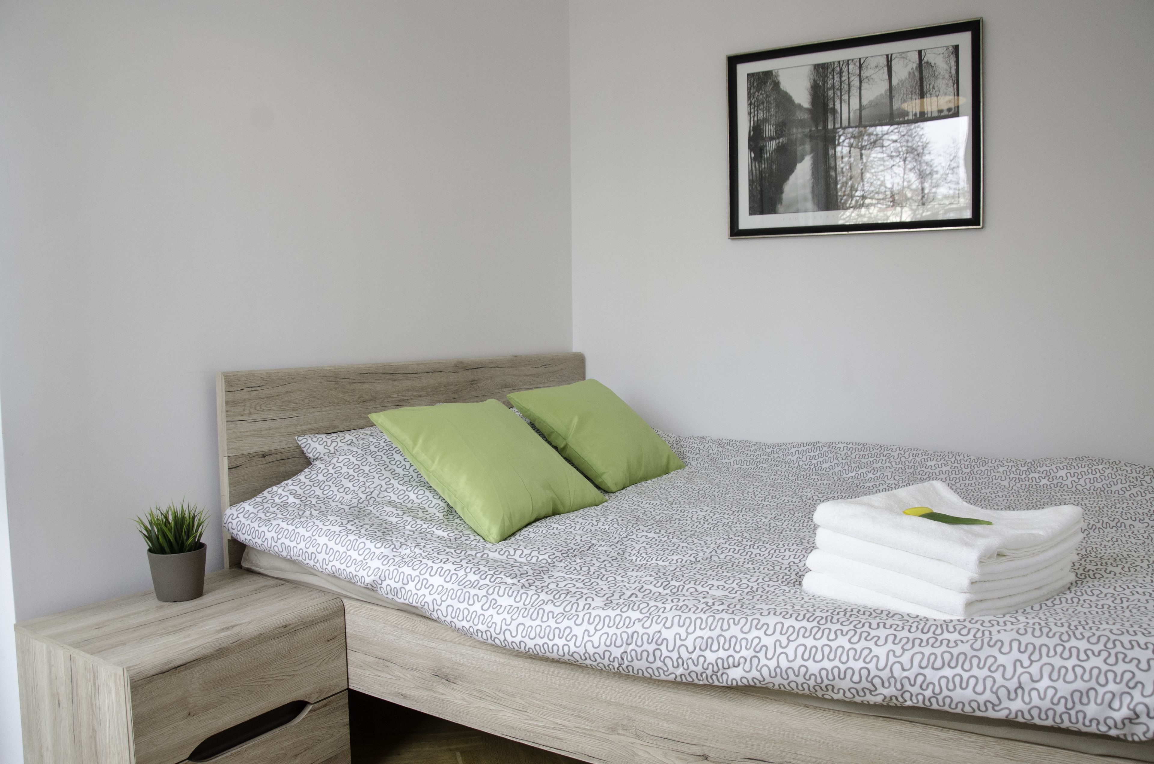 Un lit bien fait, recouvert d’une couvre-lit à motifs, avec deux oreillers verts et une pile de serviettes blanches sur le côté droit.