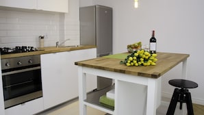 A modern kitchen with white cabinets, a stainless steel refrigerator, a wooden countertop, and a small table with a bottle of wine and lemons. - Bizzi LuxHeart of Old Town Apartment (Warsaw)