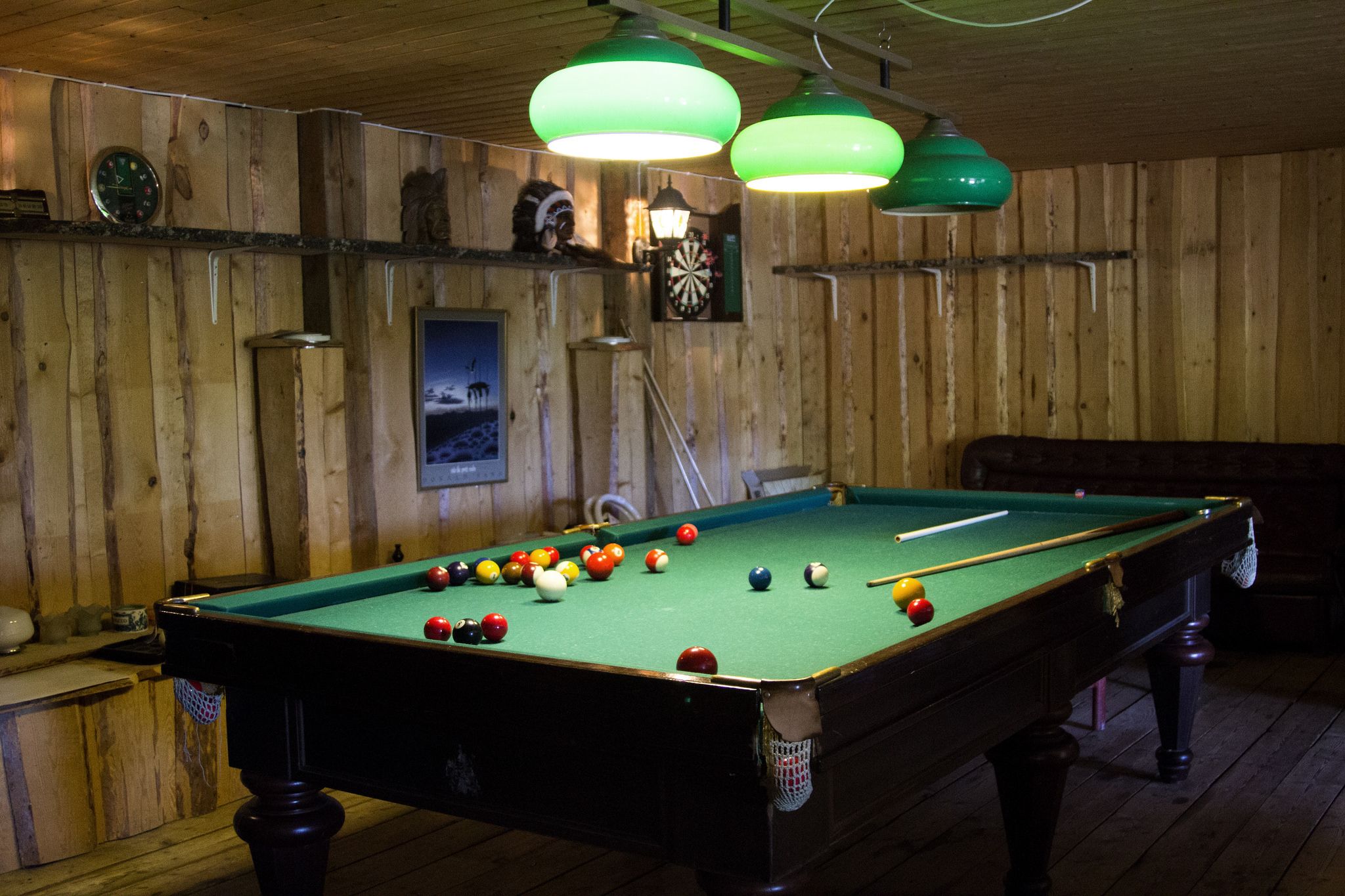 A pool table with balls, a dartboard, and a clock on the wall.