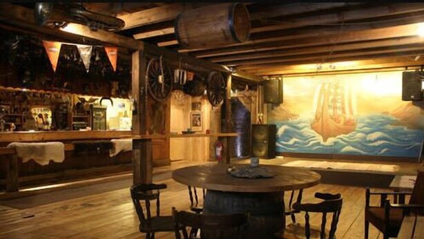 Un espace bar avec des meubles en bois, une grande fresque représentant un navire et une table ronde au centre.
