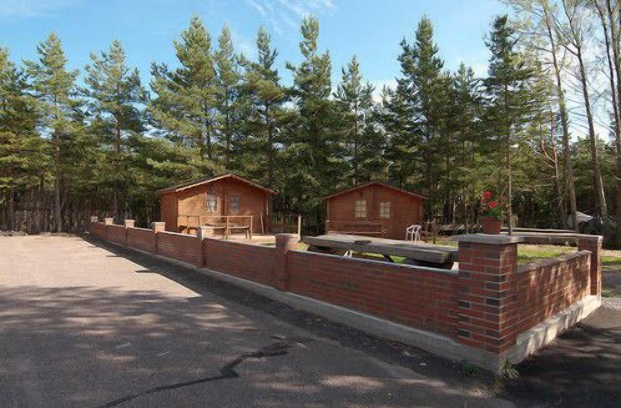 A rustic cabin with a brick foundation and a wooden structure, surrounded by a forested area.