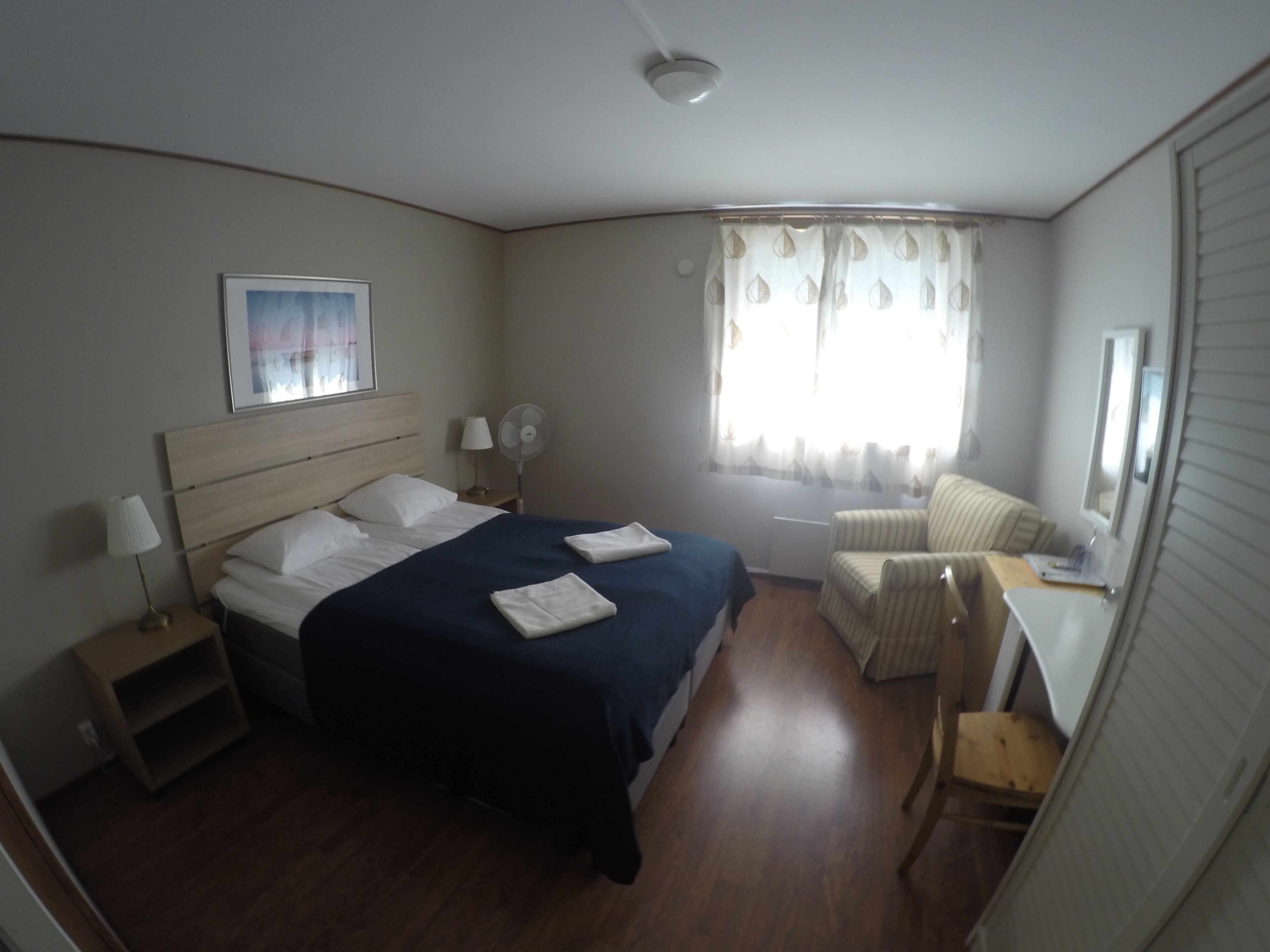 Un dormitorio con cama, mesitas de noche, un escritorio, una silla, una ventana con cortinas y un ventilador de techo.