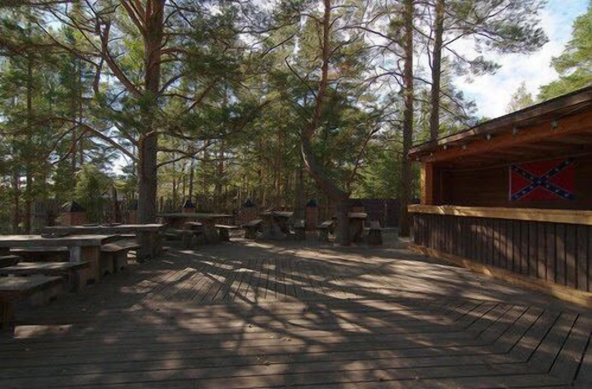 An outdoor wooden deck with picnic tables and a covered area with a flag.
