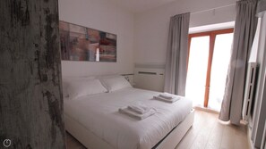 A modern bedroom with a large bed, a bedside table, a wall-mounted heater, and a window with curtains. - Italianway   - Bligny 39 Studio (Milan)