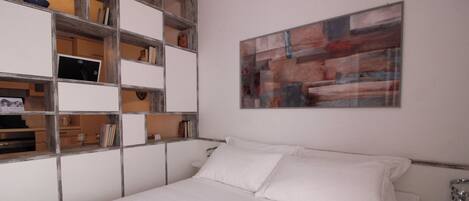 A bedroom with a bed, a built-in bookshelf, and a wall-mounted abstract painting.