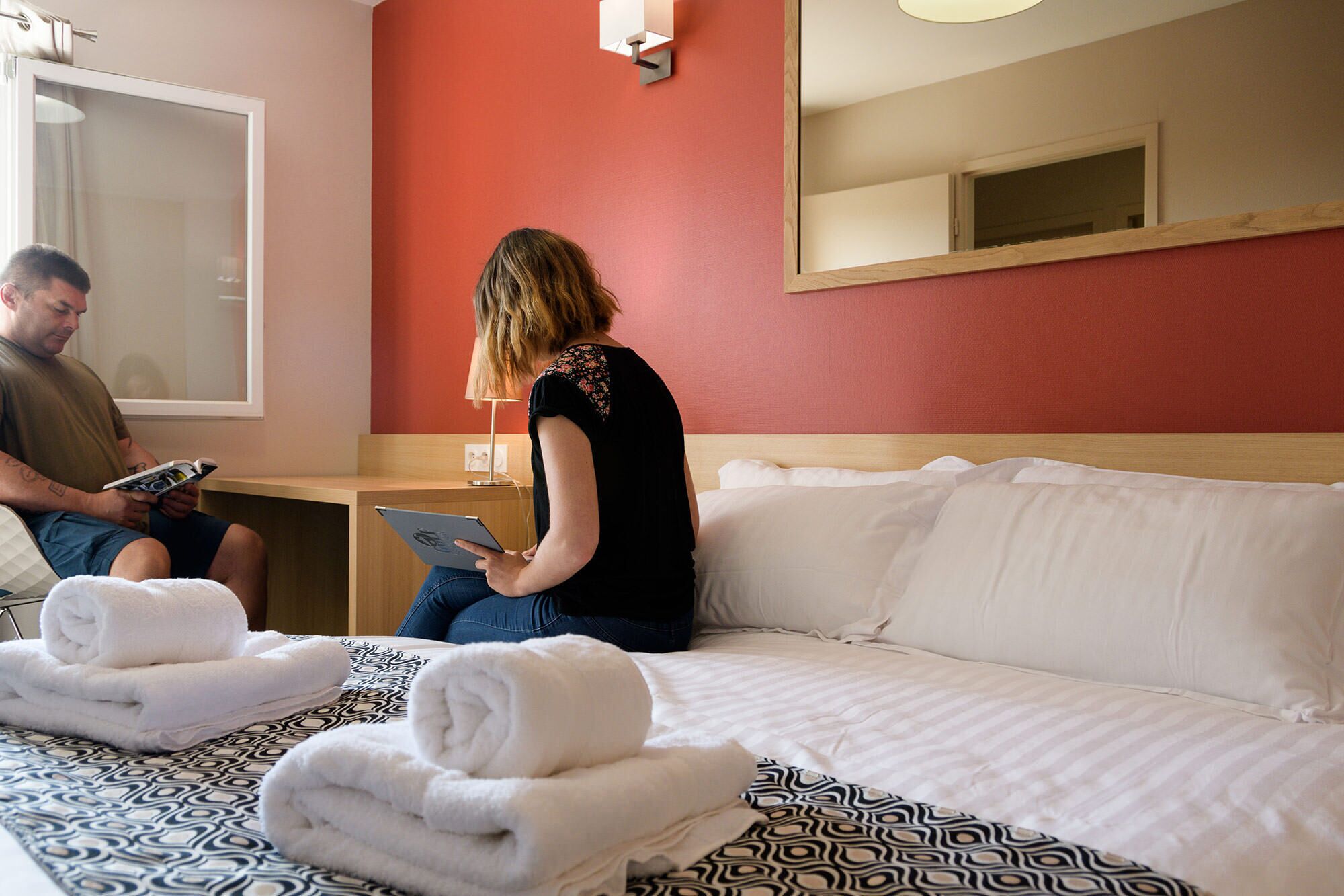 A hotel room with a bed, a bedside table, a mirror, and a window.