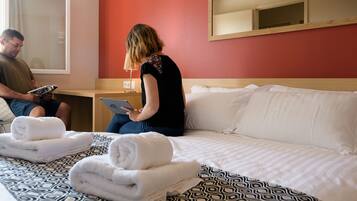 A hotel room with a bed, a bedside table, a mirror, and a window.
