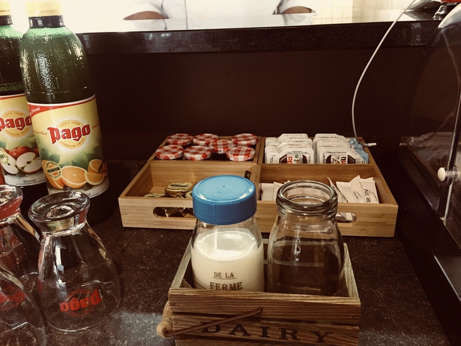 Un comptoir de cuisine avec divers aliments et condiments, notamment des bouteilles de jus de fruits, des pots de miel et une boîte en bois étiquetée « PRODUITS LAITIERS ».