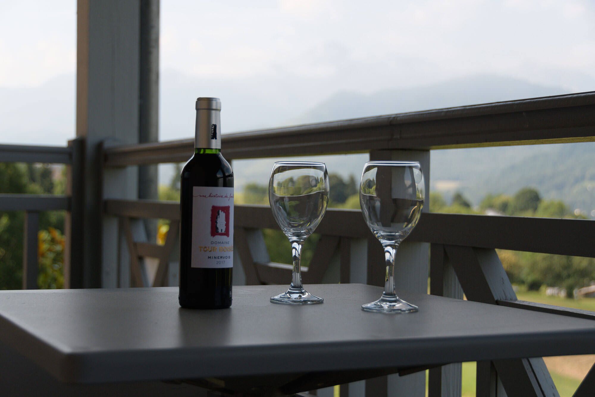 A bottle of wine and two glasses on a table with a view of mountains.