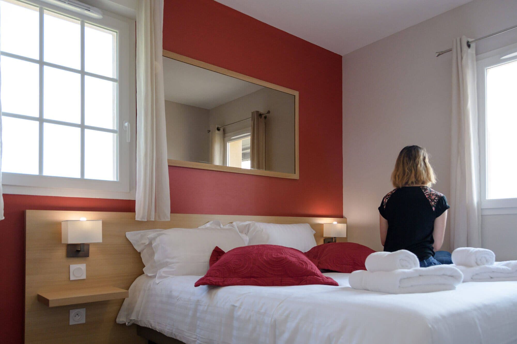 Una habitación de hotel con una cama, un espejo grande y un ventanal con cortinas.