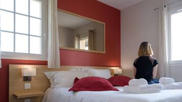 Una habitación de hotel con una cama, un espejo grande y un ventanal con cortinas.