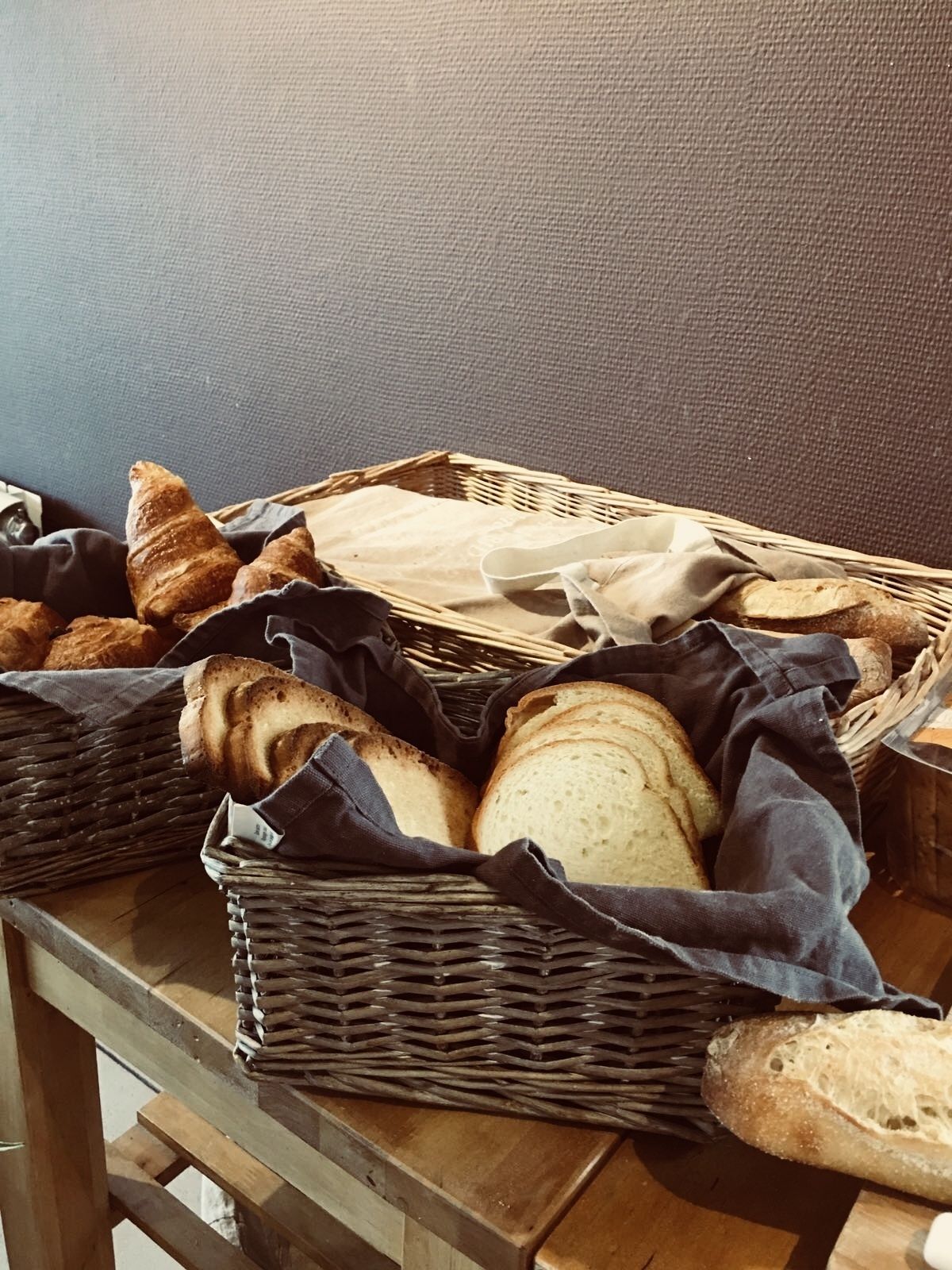 A wicker basket filled with various types of bread on a wooden table.
