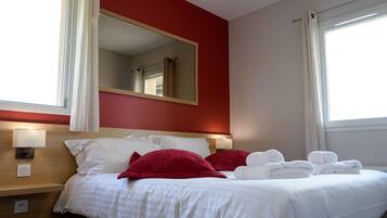 A hotel room with a bed, two bedside lamps, a mirror, and a window with curtains.