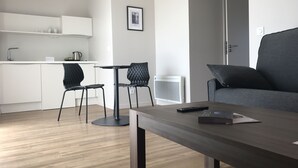 Un espacio habitable moderno con comedor, un sofá gris y una cocina al fondo.