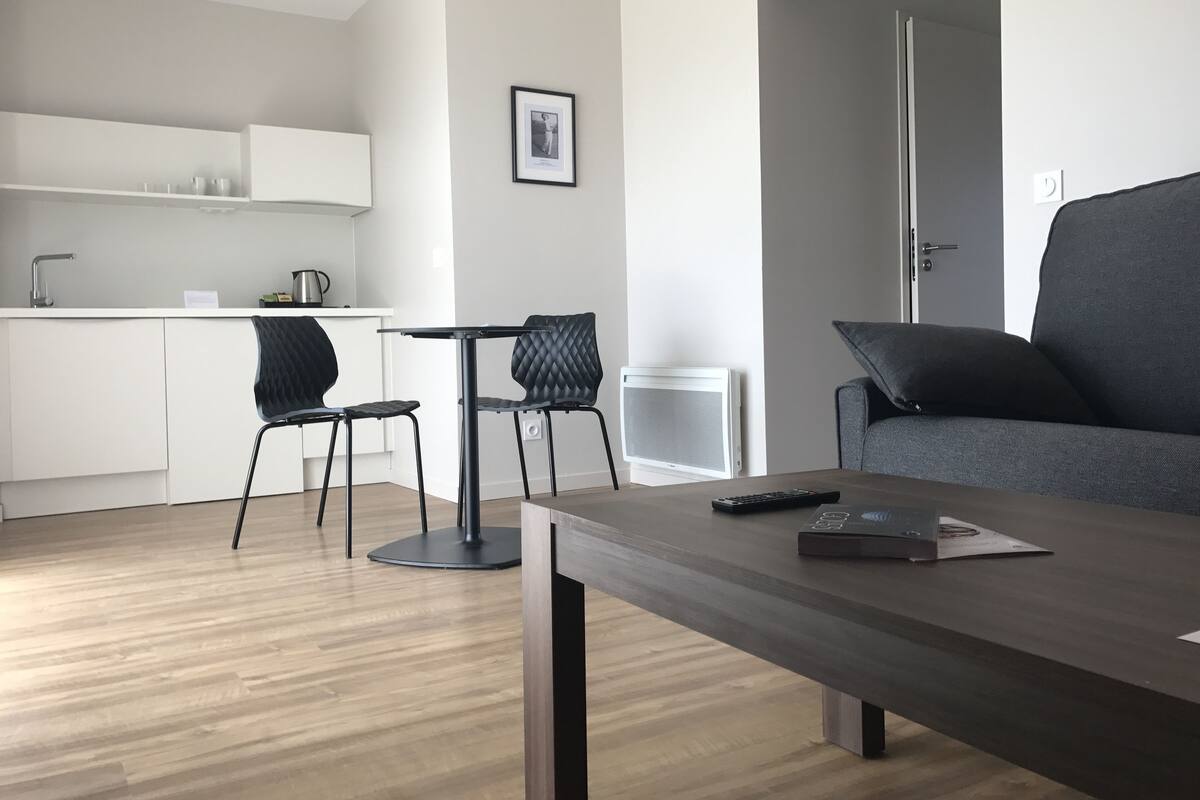 A modern living space with a dining area, a gray sofa, and a kitchen in the background.