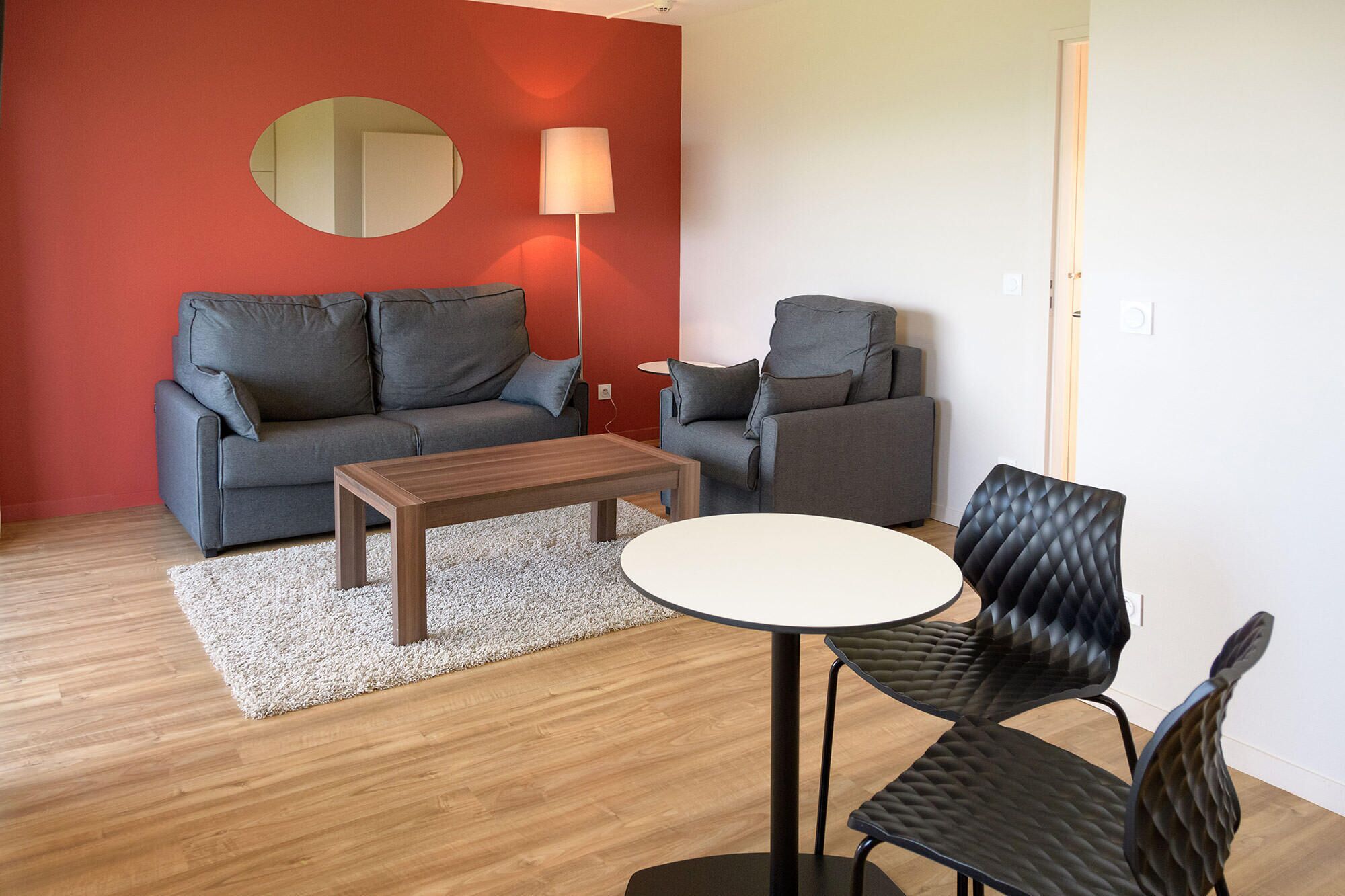 A modern living room with a grey sofa, a smaller grey armchair, a wooden coffee table, and a black cushioned chair.