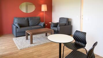 A modern living room with a grey sofa, a smaller grey armchair, a wooden coffee table, and a black cushioned chair.