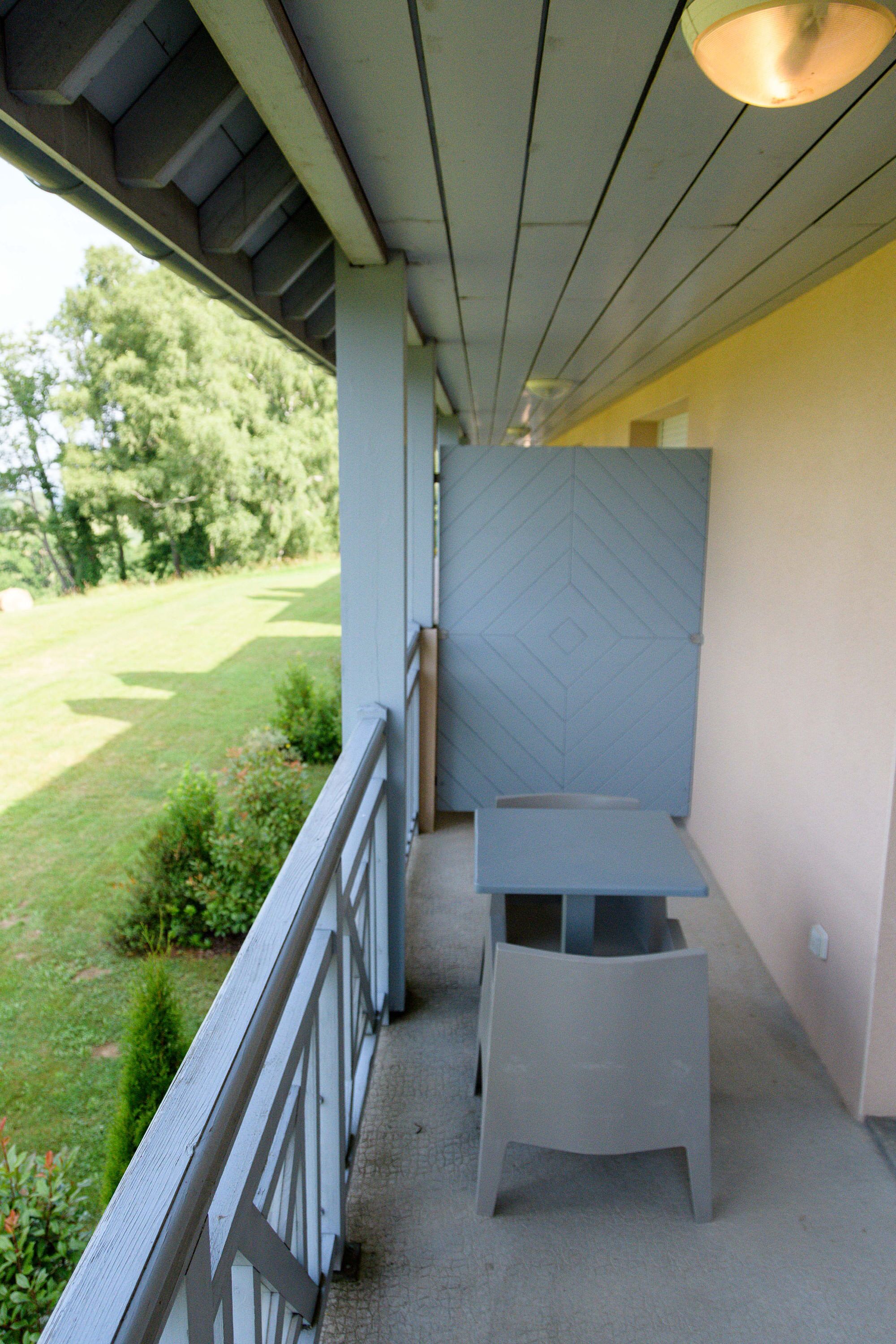 Eine überdachte Veranda mit Tisch und Stuhl, Blick auf eine Rasenfläche und eine Tür mit geometrischem Muster.