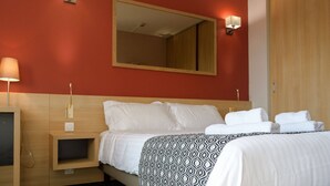 Una habitación de hotel con cama, mesitas de noche, un espejo y lámparas de pared.