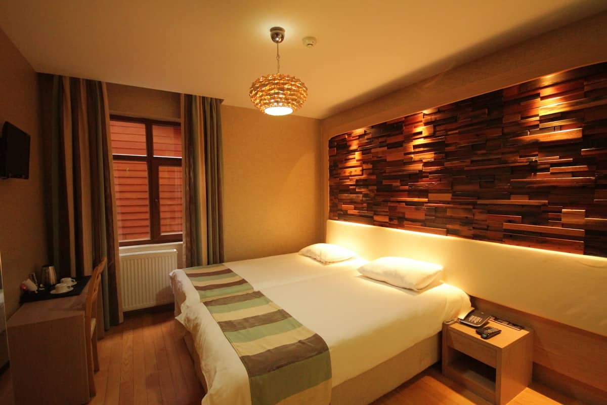Quarto de hotel com cama, mesa de cabeceira, luminária e parede com design de painel de madeira.