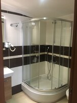 Cabina de ducha con paredes de vidrio, un cabezal de ducha manual y un grifo empotrado.