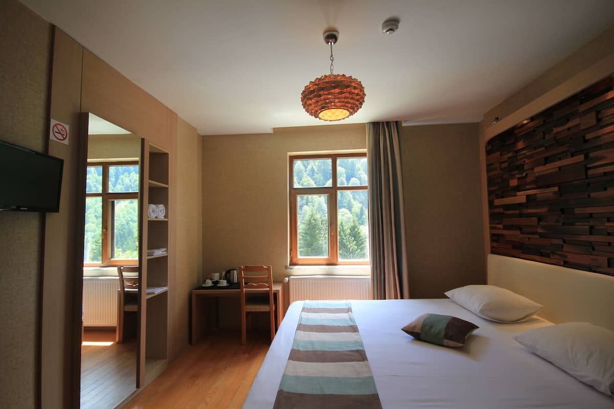 Quarto com cama, escrivaninha, cadeira e janela com vista para árvores.