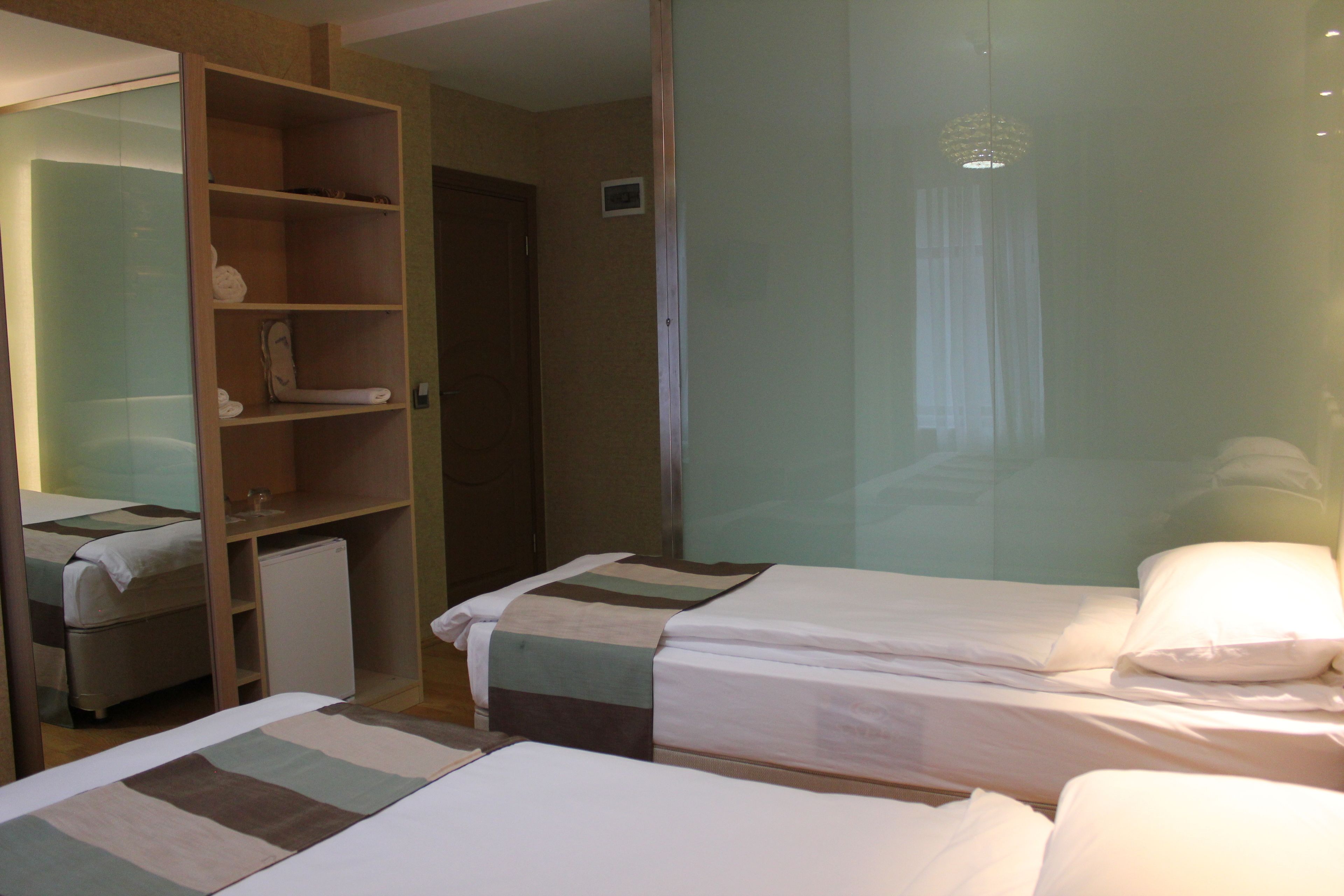 Habitación de hotel con dos camas, un armario, un refrigerador pequeño y cabina de ducha de vidrio.