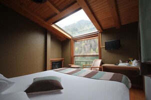 A bedroom with a large bed, a desk with a chair, a television, and a skylight.