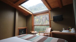 A hotel room with a bed, a desk, a chair, a television, a fireplace, and a large window with a view of trees. - Ayderoom Otel (Camlihemsin)