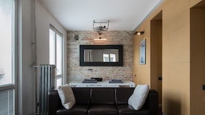Una sala de estar moderna con una pared de ladrillo, un sofá de cuero negro, una mesa de centro blanca y un espejo grande.