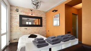 Una habitación de hotel moderna con pared de ladrillo, una cama grande, una mesita de noche blanca con toallas, un espejo y un cartel para el Festival Internacional de Cortometrajes.