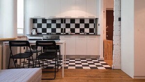 A compact kitchen with white cabinets, a black and white checkered floor, and a small dining area with two chairs. - Bizzi LuxProchnika Studio (Warsaw)